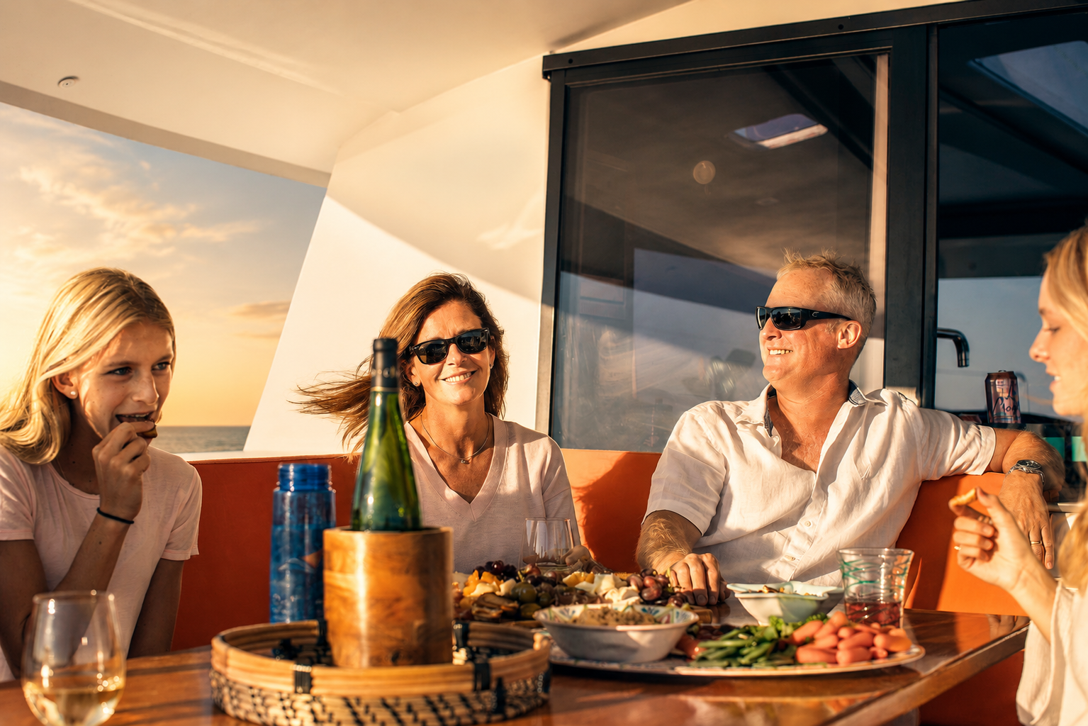 Family and friends enjoying food and drinks together during a private captained sailing charter at sunset